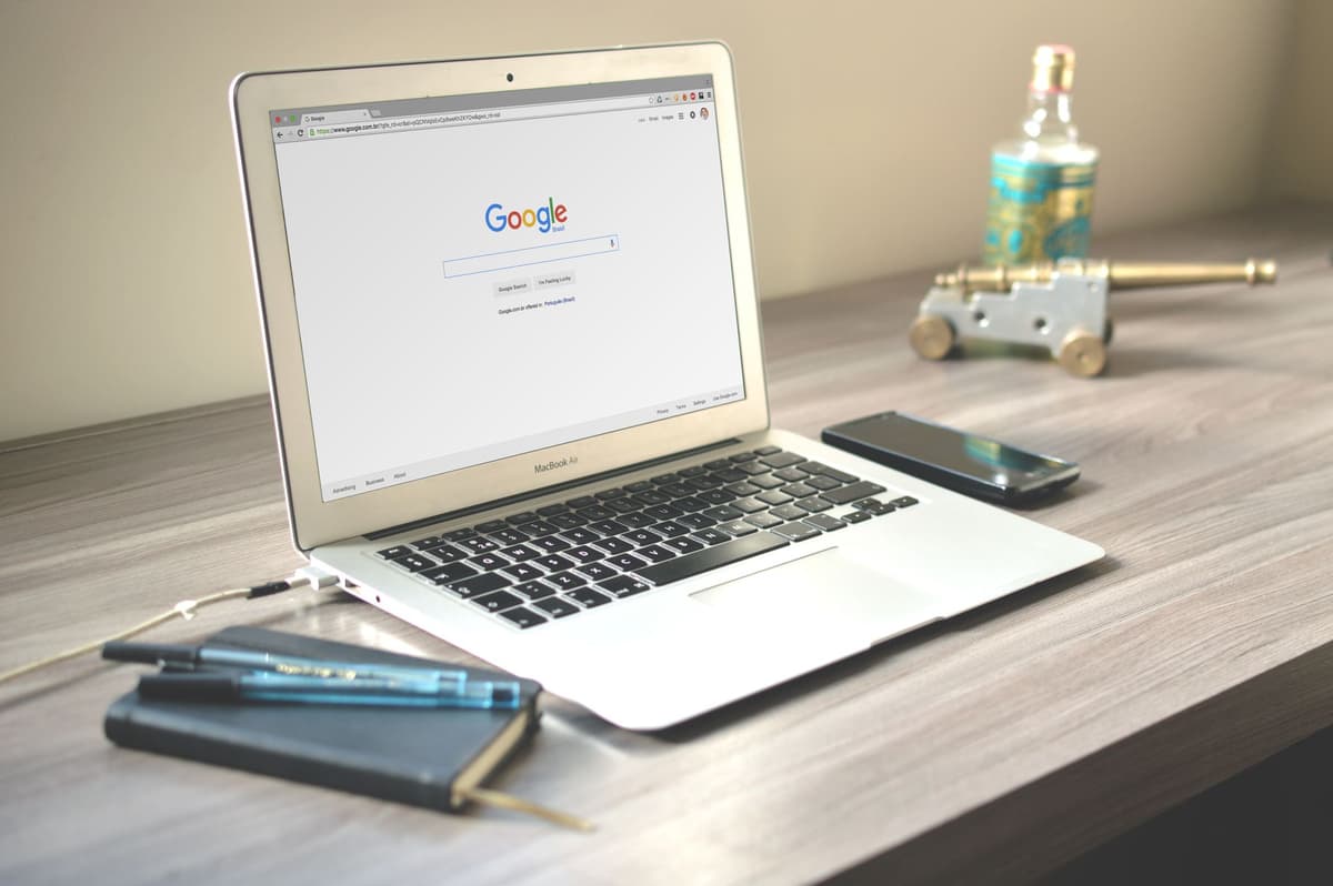 google ads beheer — A neat workspace featuring a laptop displaying Google search, a smartphone, and a notebook on a wooden desk.